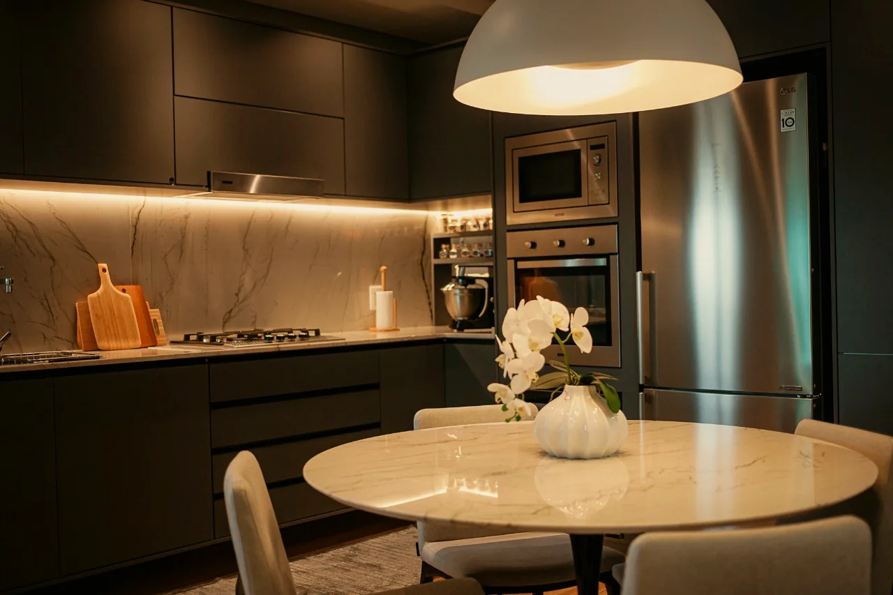 Cozinha do apartamento AK605, com marcenaria escura, backsplash em mármore e pendente sobre a mesa